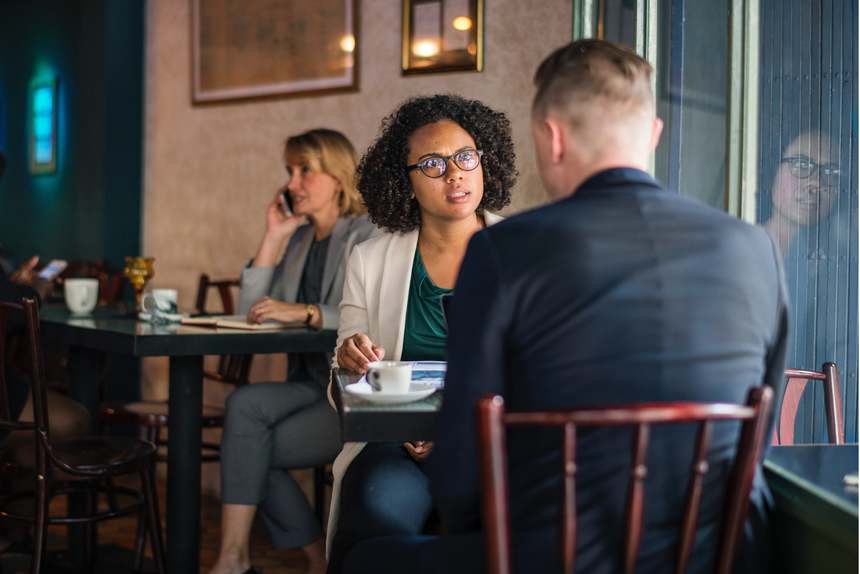 Two professionals talking in a coffee shop about how to deal with backstabbing coworkers