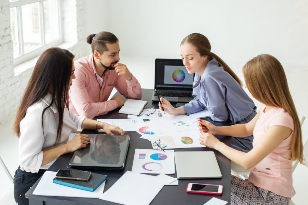 four people sitting around a table with papers and laptop while having a meeting