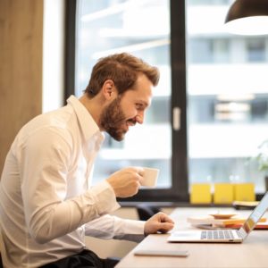 man sitting researching for interview tools on his laptop while drinking coffee