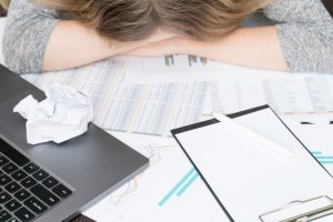 woman whose promotion got rejected lies with her head on a desk in front of a computer in the office