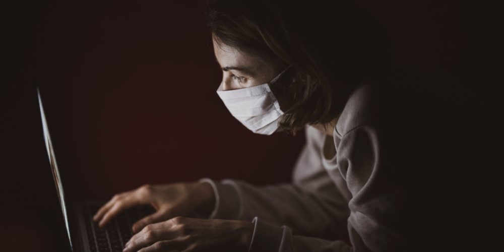 Woman with face mask using laptop during coronavirus pandemic