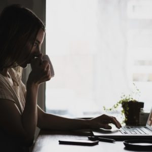 Woman sipping coffee while writing a professional resume in her laptop